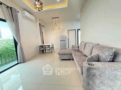 Modern living room with stylish gray sofa and dining area, featuring elegant lighting and natural light from large windows.