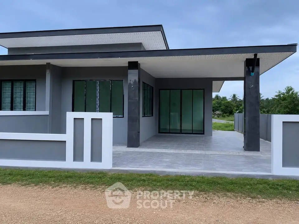 Modern single-story house with sleek design and spacious porch, surrounded by greenery.