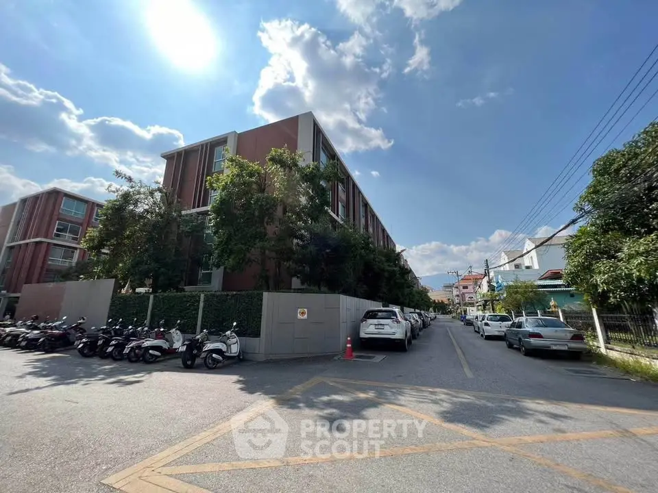 Modern residential building with parking and lush greenery under a clear blue sky.