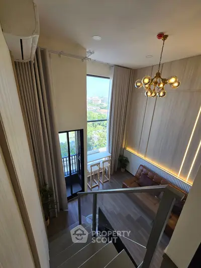 Stunning loft-style living room with high ceilings and modern chandelier, featuring a cozy seating area and large window view.