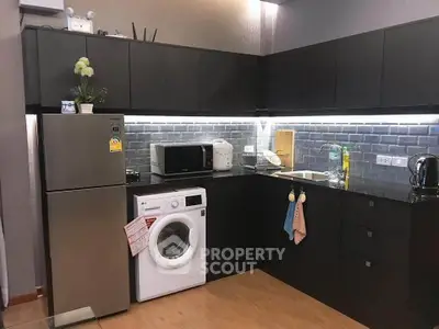 Modern kitchen with sleek black cabinets, washing machine, and stainless steel fridge in a stylish apartment.