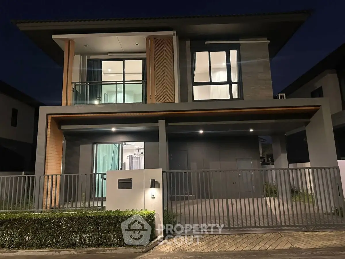 Modern two-story house with sleek design and gated entrance at night.