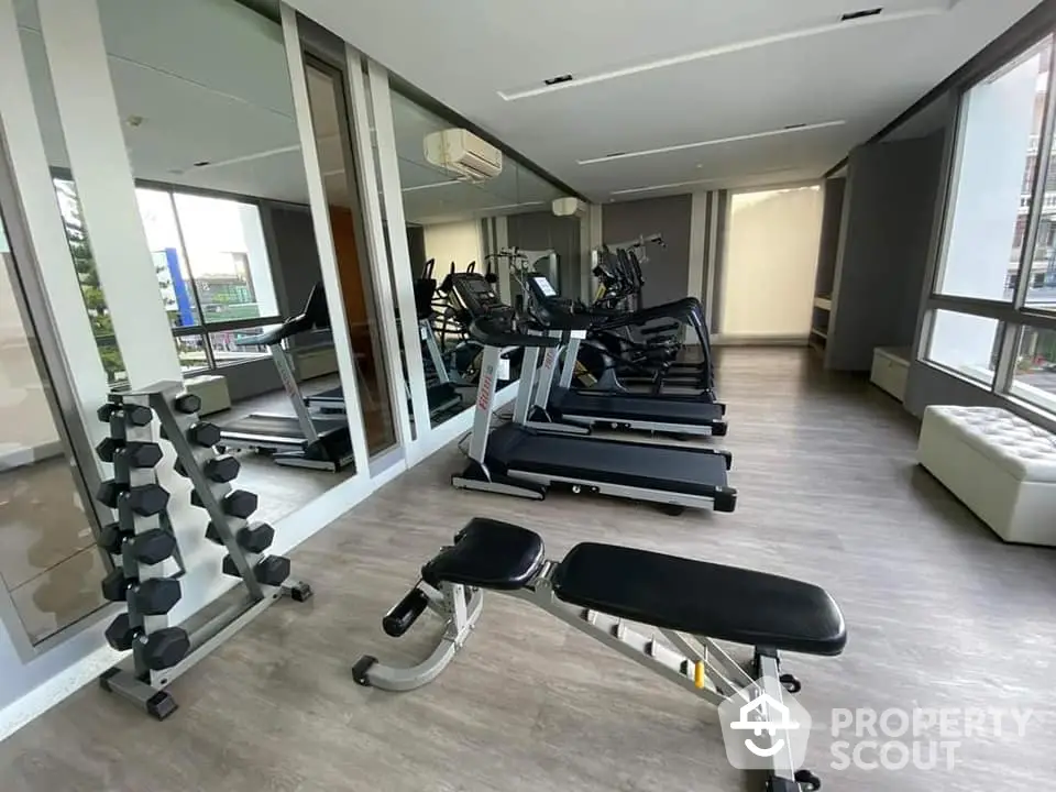 Spacious and modern gym facility in a residential building with state-of-the-art treadmills, free weights, and ample natural light.