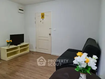 Cozy living room with modern decor and wooden flooring, featuring a sleek black sofa and a flat-screen TV.