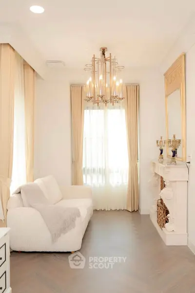 Elegant living room with chandelier and fireplace, featuring a cozy white sofa and luxurious decor.