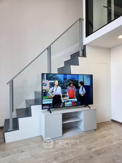 Modern duplex interior with sleek staircase and TV setup, showcasing contemporary design and open space.