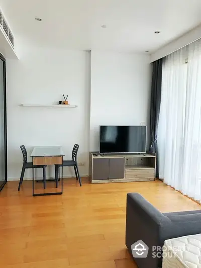 Modern living room with sleek furniture and large TV, featuring wooden flooring and natural light.