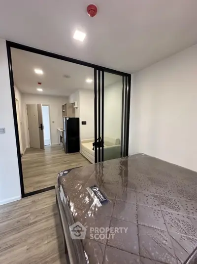 Modern apartment interior with bedroom and living area separated by glass doors, featuring sleek design and wood flooring.