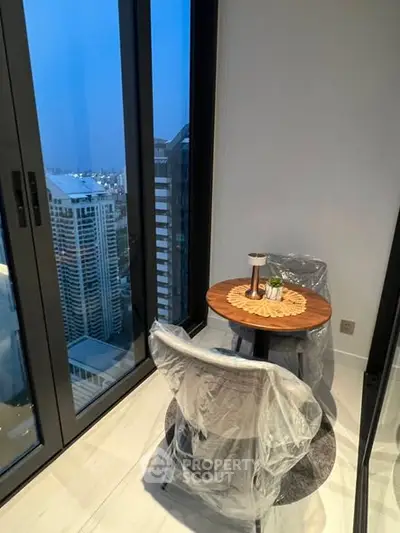 Chic urban balcony with city view, featuring cozy seating and modern glass doors.