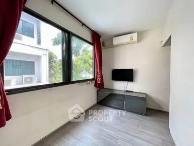 Bright living room with large window, red curtains, air conditioning, and wall-mounted TV.