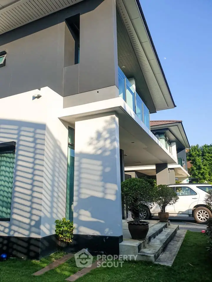 Modern two-story house with sleek design and lush greenery, featuring a spacious balcony and contemporary architecture.