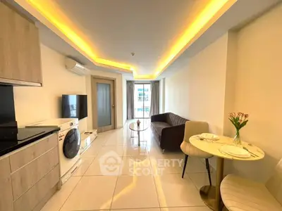 Modern living room with stylish furniture and open kitchen layout, featuring a washing machine and elegant lighting.