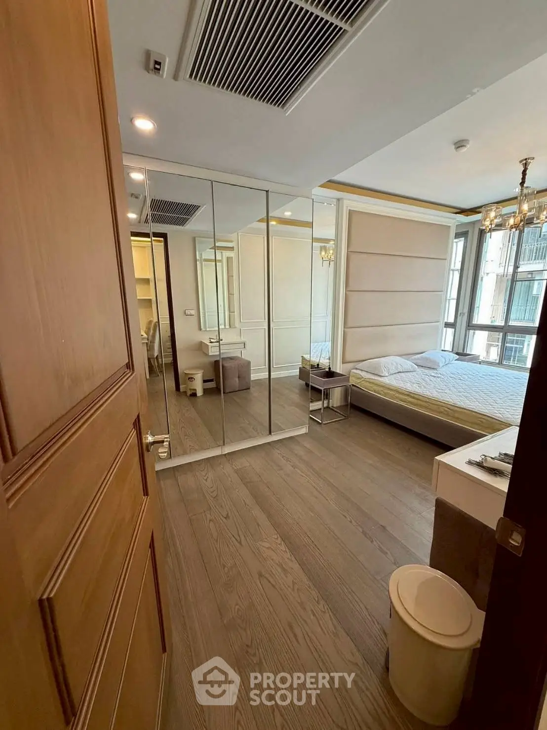 Spacious bedroom with mirrored closet and elegant chandelier in modern apartment