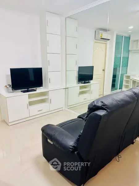 Modern living room with sleek black sofa and mirrored wall enhancing space.