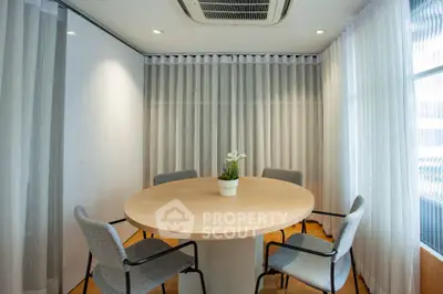 Modern meeting room with round table and elegant chairs, featuring natural light and stylish curtains.