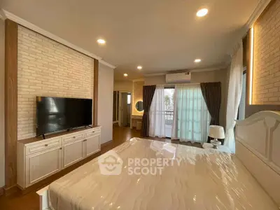 Spacious bedroom with modern decor and natural light, featuring a large TV and elegant furnishings.