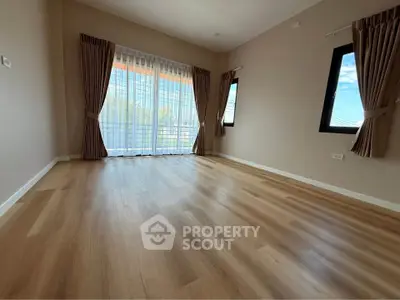 Spacious empty room with wooden flooring and large windows for natural light.
