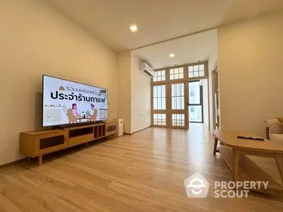 Spacious modern living room with wooden flooring and large TV, perfect for relaxation.