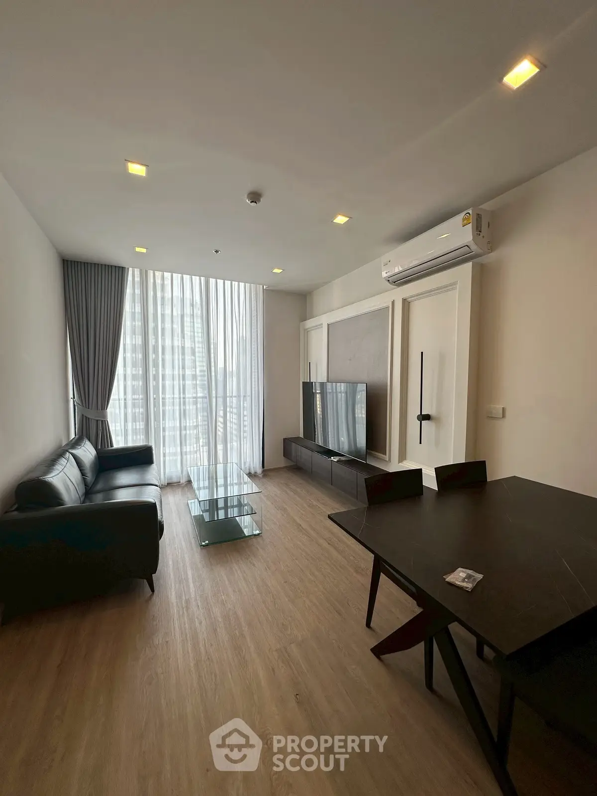 Modern living room with sleek furniture and large window offering city views.