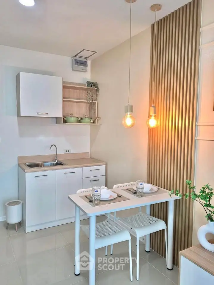 Modern kitchen with sleek white cabinets and cozy dining area, featuring stylish pendant lighting and wooden accents.