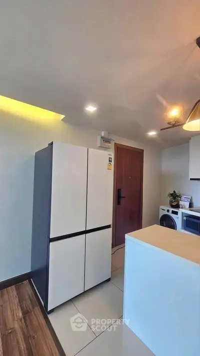 Modern kitchen with sleek fridge and stylish lighting in a contemporary apartment.