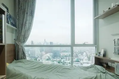 Cozy bedroom with panoramic city view from large window, perfect for urban living.