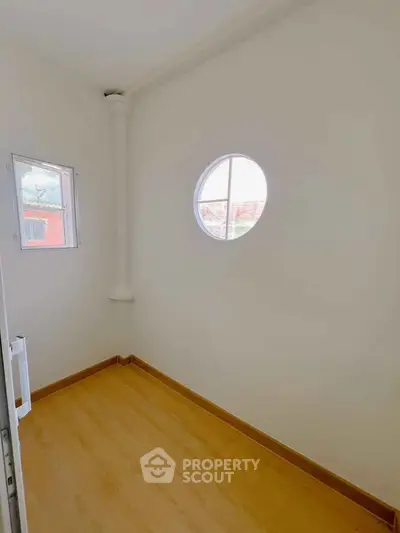Bright small room with circular window and wooden flooring