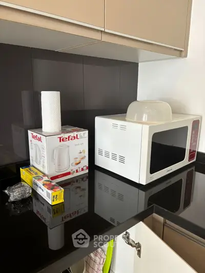 Modern kitchen corner with microwave and Tefal kettle box on sleek countertop.