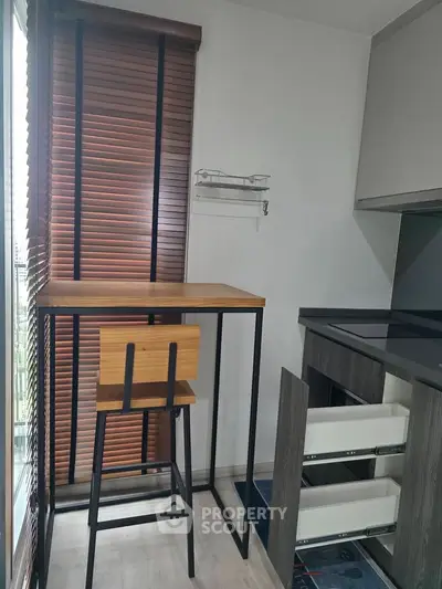 Modern kitchen with sleek cabinetry, high table and chair, and large window with blinds.