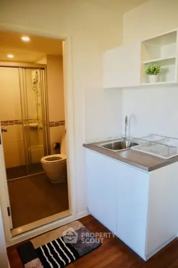 Compact bathroom with modern fixtures adjacent to a small kitchenette.