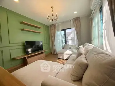 Elegant living room with green accent wall and chandelier, featuring cozy sofa and large windows.