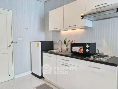 Modern kitchen with sleek white cabinets, compact fridge, and microwave in a stylish apartment.