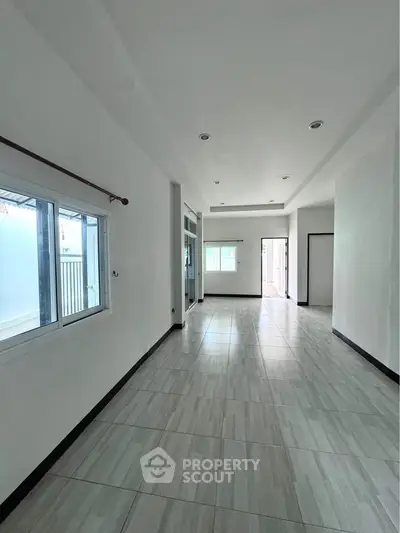Spacious empty room with tiled flooring and large windows, perfect for customization.