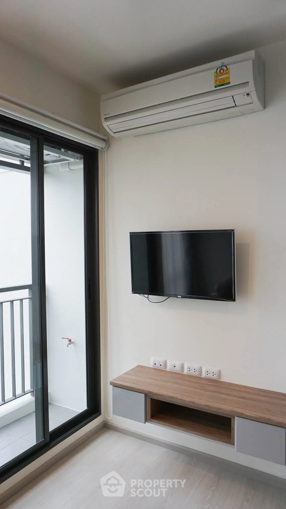 Modern living room with wall-mounted TV and air conditioning, adjacent to a balcony with sliding glass doors.