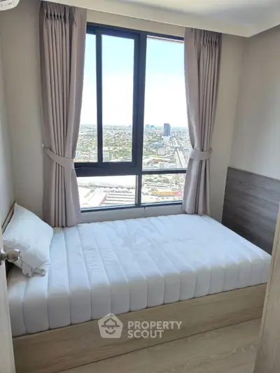 Cozy bedroom with stunning city view from high-rise window, featuring modern decor and natural light.