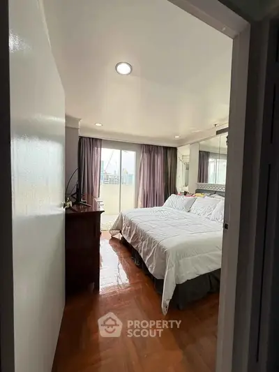 Spacious bedroom with large windows and elegant wooden flooring.