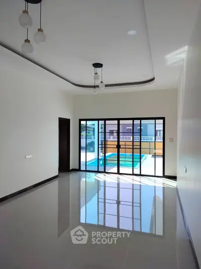 Spacious living room with large windows and pool view, modern lighting, and glossy tiled floor.
