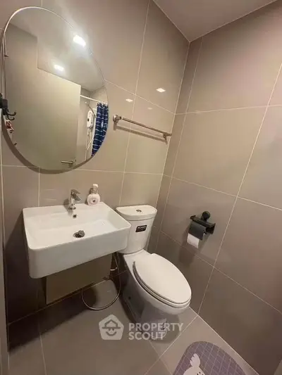Modern bathroom with sleek fixtures and neutral tiles, featuring a round mirror and compact sink.
