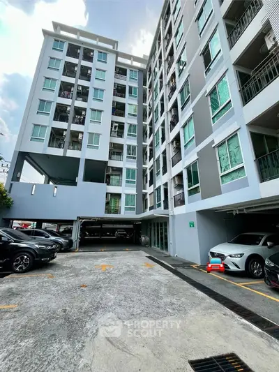 Modern multi-story apartment building with parking area and sleek design.