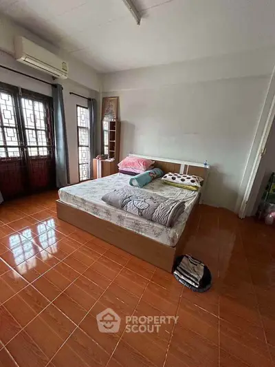 Spacious bedroom with large bed and natural light from window, featuring tiled flooring and air conditioning.