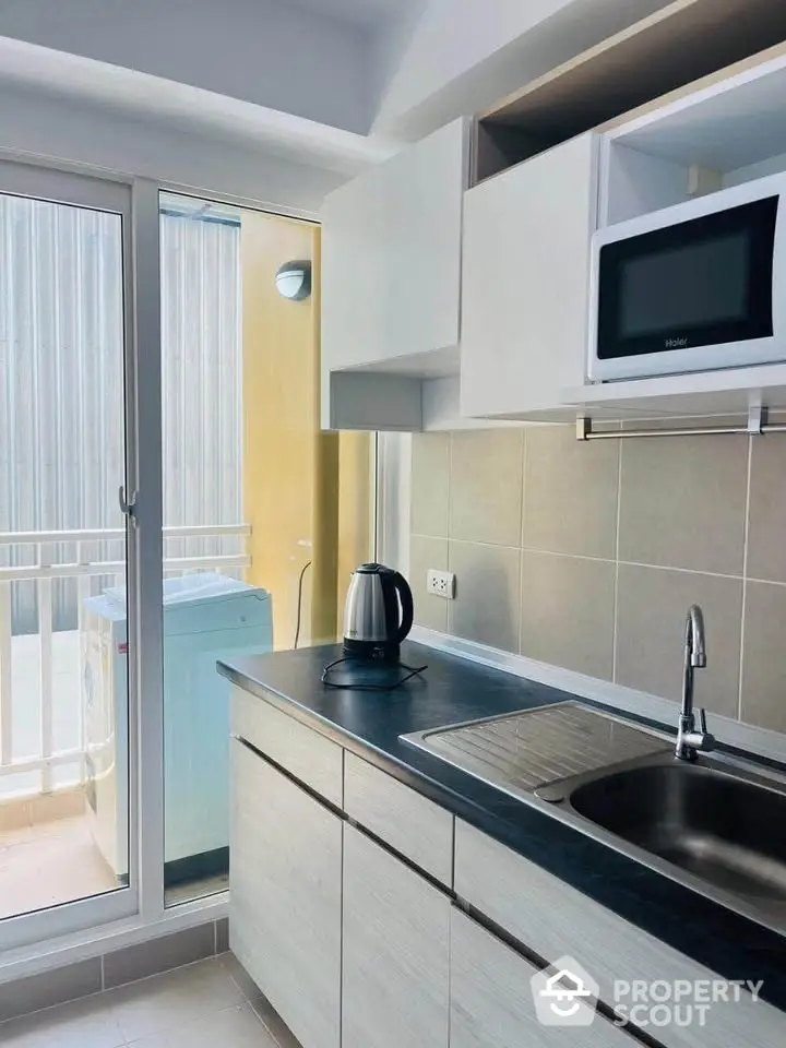 Modern kitchen with sleek cabinetry, microwave, and balcony access for natural light.