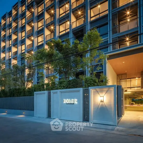 Modern condominium building exterior with illuminated facade and lush greenery.