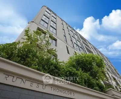 Modern high-rise building with lush greenery and clear blue sky in Thonglor 5.