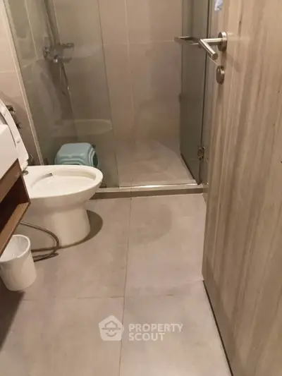 Modern bathroom with glass shower and washing machine, featuring sleek tile flooring.