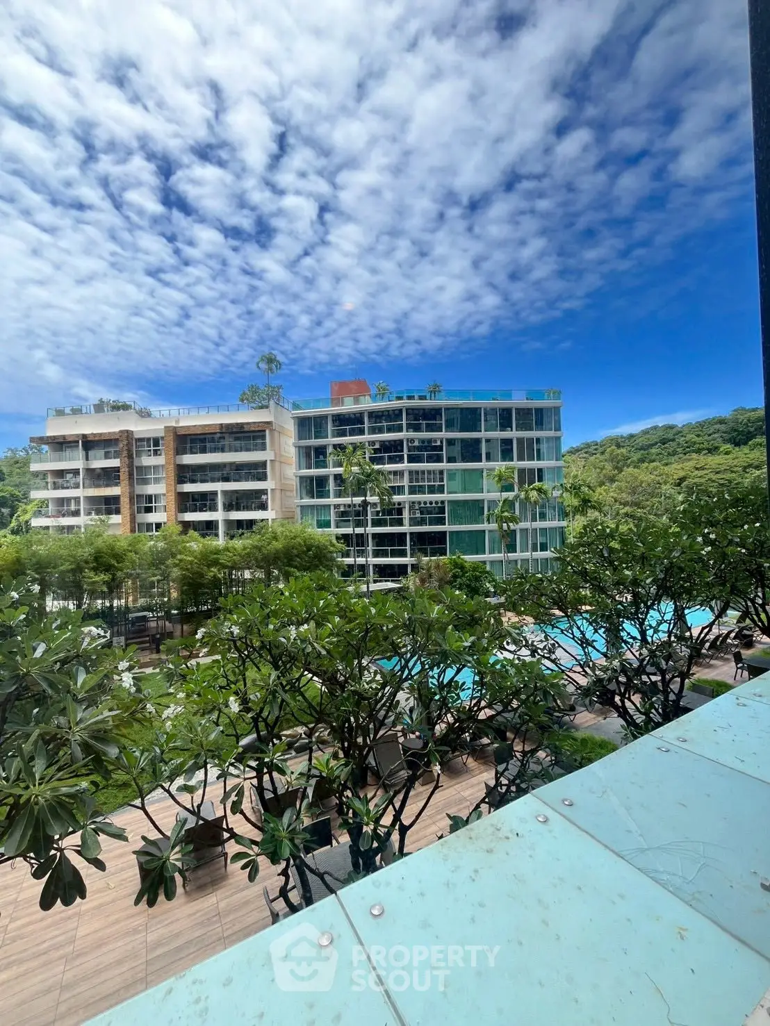 Luxurious apartment complex with pool and lush greenery under a vibrant blue sky.