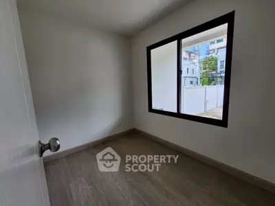 Spacious empty room with large window and wooden flooring in modern home.