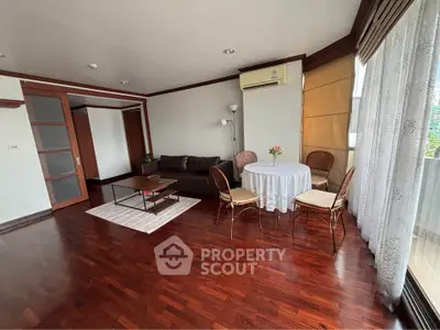 Spacious living room with hardwood floors, cozy seating, and natural light from large windows.