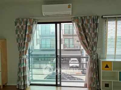 Modern living room with large window and air conditioning, offering a view of the urban neighborhood.