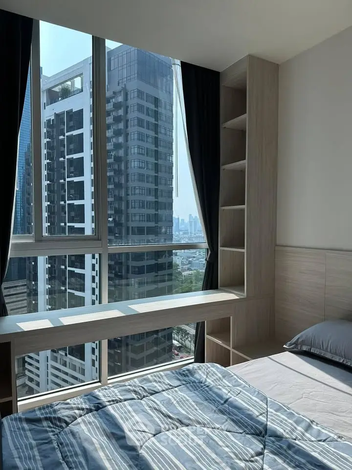 Modern bedroom with large windows offering stunning city views in a high-rise building.