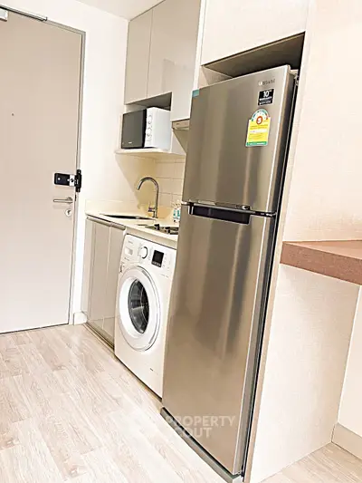 Modern kitchen with stainless steel fridge and washing machine in compact layout.